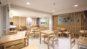 A spacious dining area with multiple wooden tables and chairs, a glass partition with decorative elements, and a modern ceiling design. - Super OYO 483 Pannee Hotel Khaosan (Bangkok)