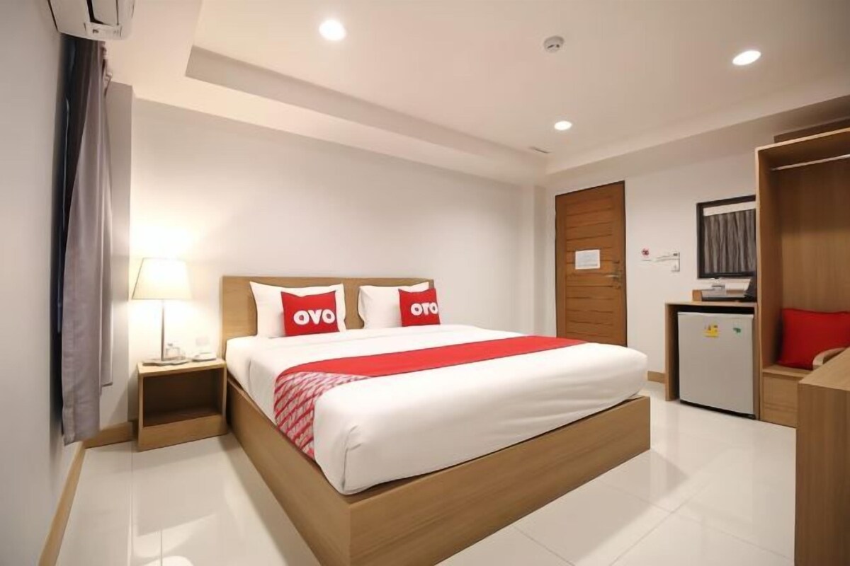 Una habitación de hotel con cama, mesita de noche, escritorio, armario y un refrigerador pequeño.