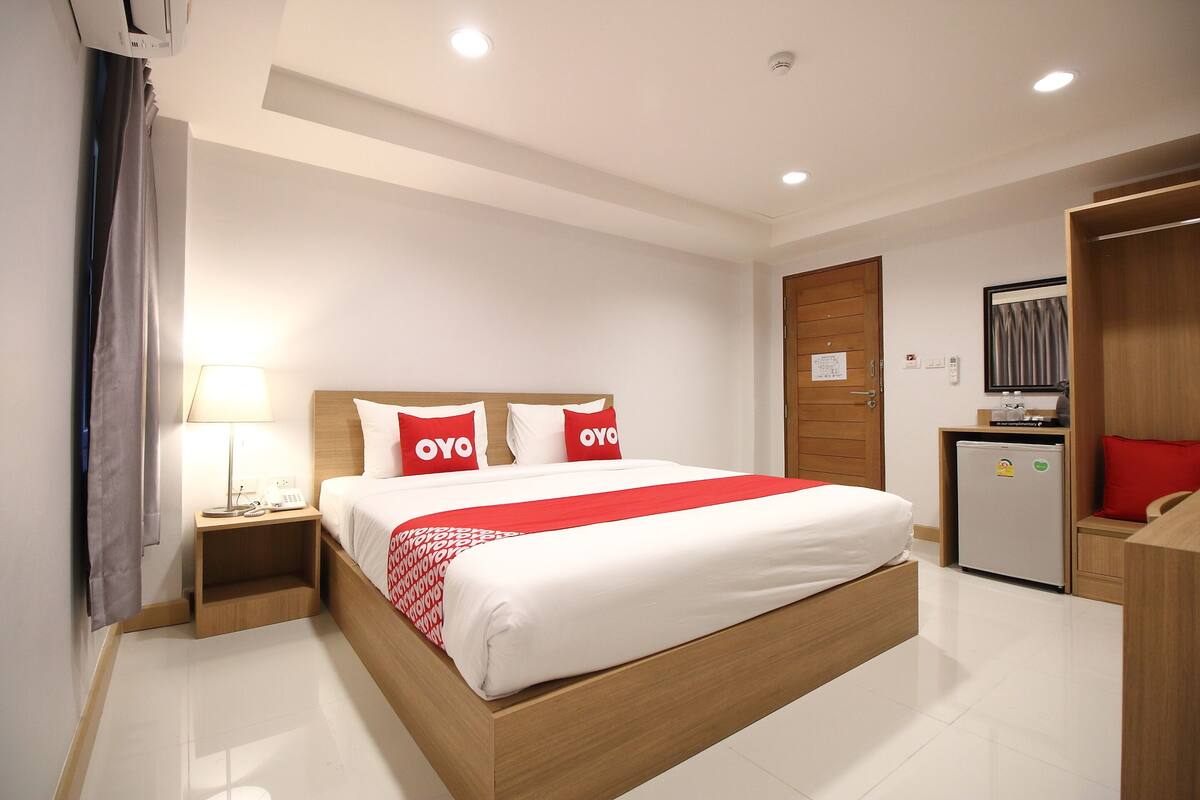 Une chambre d’hôtel avec un grand lit, une table de chevet avec une lampe, un petit réfrigérateur et une armoire en bois.