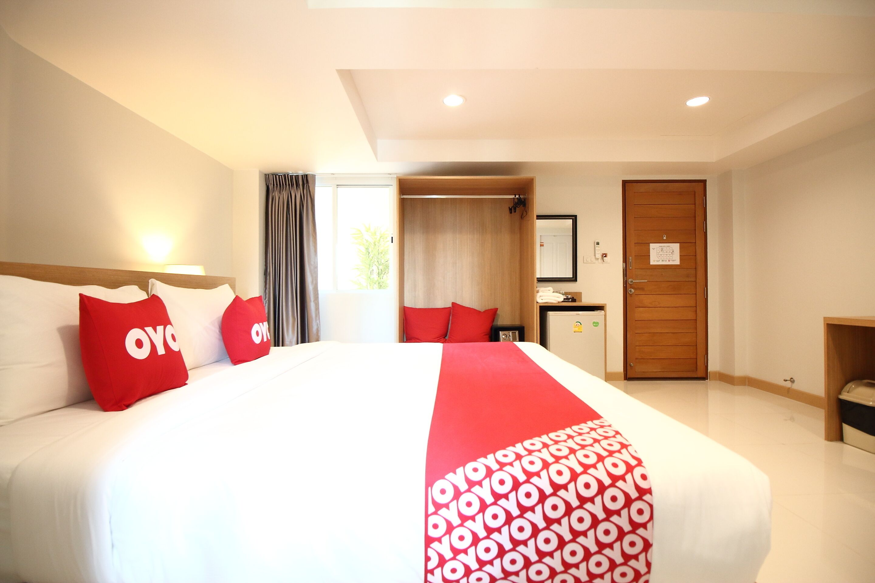 A hotel room with a large bed, red pillows, a wooden door, and a small desk.