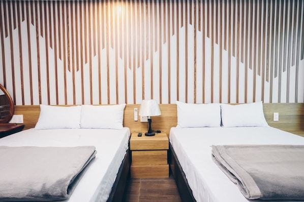 A hotel room with two beds, a wooden headboard, a nightstand with a lamp, and a wall with vertical wooden slats.