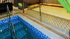 A modern indoor swimming pool with a tiled floor, a staircase with a railing, and a ceiling light fixture.