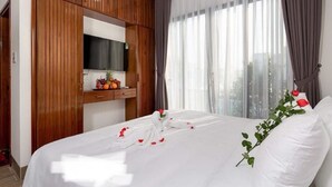 A hotel room with a bed, wooden wardrobe, a TV, and a window with curtains.