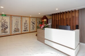 A reception area with a modern reception desk, decorative panels with traditional artwork, and a wooden partition.