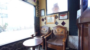 A room with two wooden chairs and a small round table, a window with a view of the street, and a wall decorated with framed certificates and a framed document. - OYO 927 Carina Hotel (Pacet)