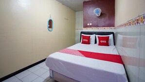 A hotel room with a bed, two red pillows, a white bedspread, and a red and white striped blanket. - OYO 927 Carina Hotel (Pacet)