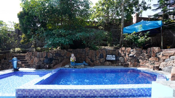 A swimming pool with a stone wall and a sign that reads "JAGALAH KERASIH." - OYO 927 Carina Hotel (Pacet)