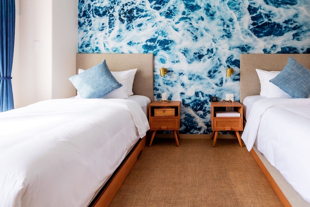 A hotel room with two beds, a marble-patterned wall, wooden nightstands, and a blue curtain.