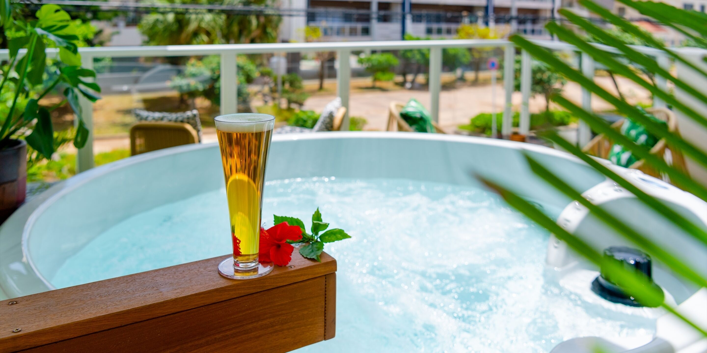 Um copo de cerveja numa prateleira de madeira ao lado de uma banheira de hidromassagem, com vista para uma varanda e vegetação.