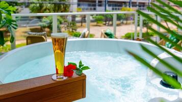 Um copo de cerveja numa prateleira de madeira ao lado de uma banheira de hidromassagem, com vista para uma varanda e vegetação.