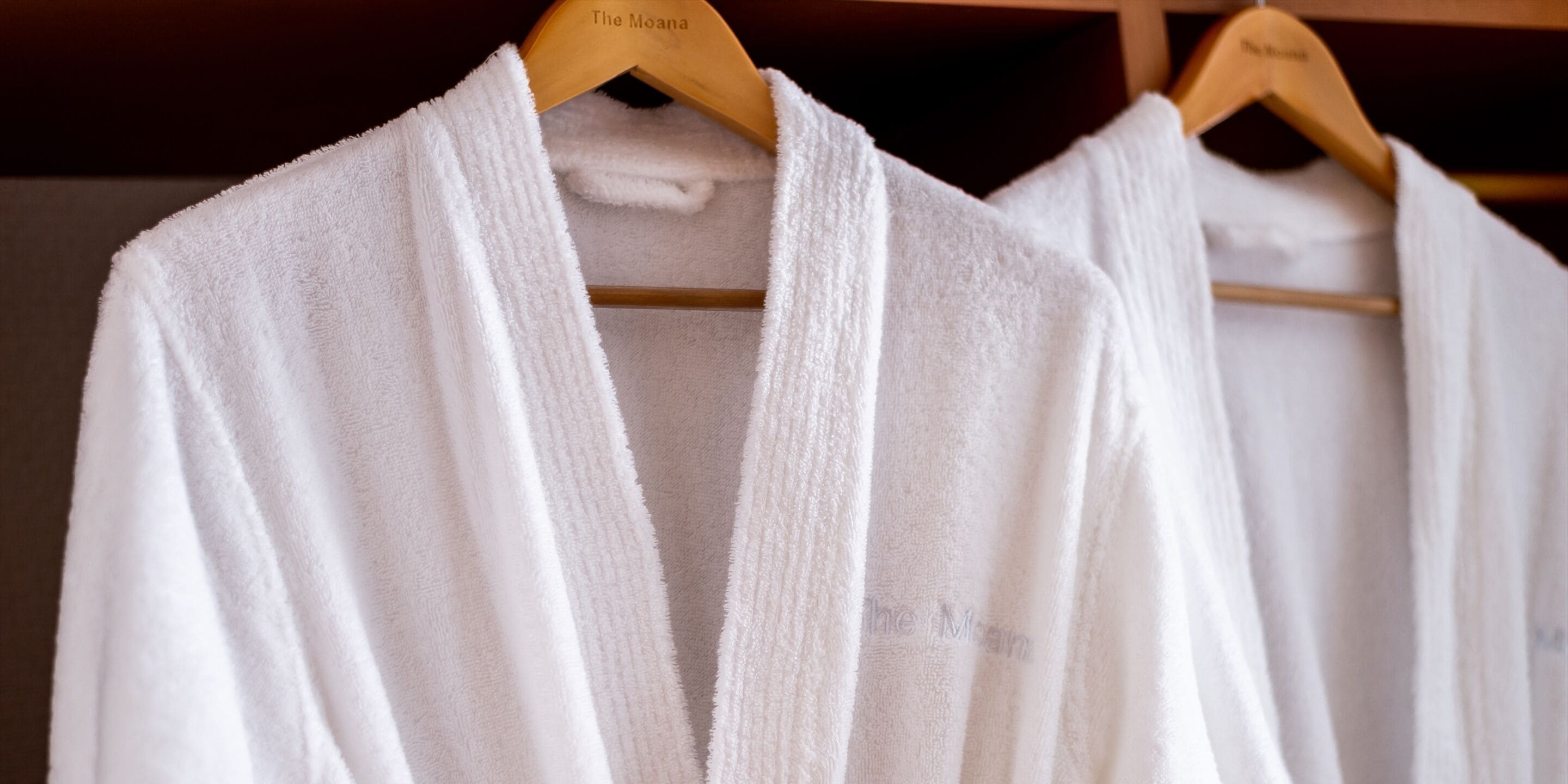 A rack of white robes hanging on wooden hangers.