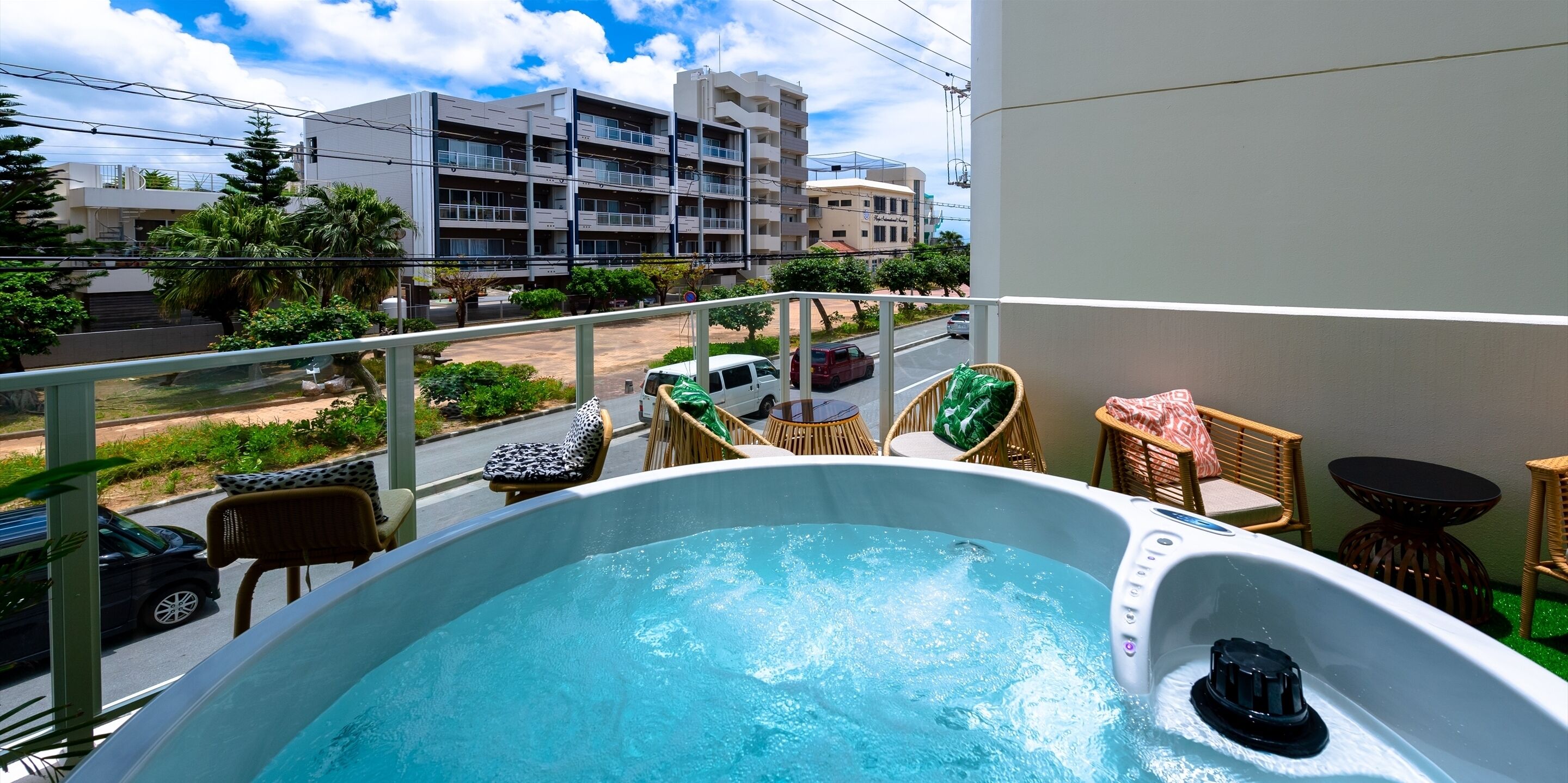 A balcony with a hot tub, wicker furniture, and a view of a street and buildings.