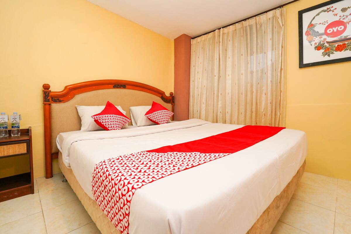 Una cama bien hecha con una colcha de cuadros rojos y blancos, un cabecero de madera y dos almohadas con un diseño rojo y blanco.