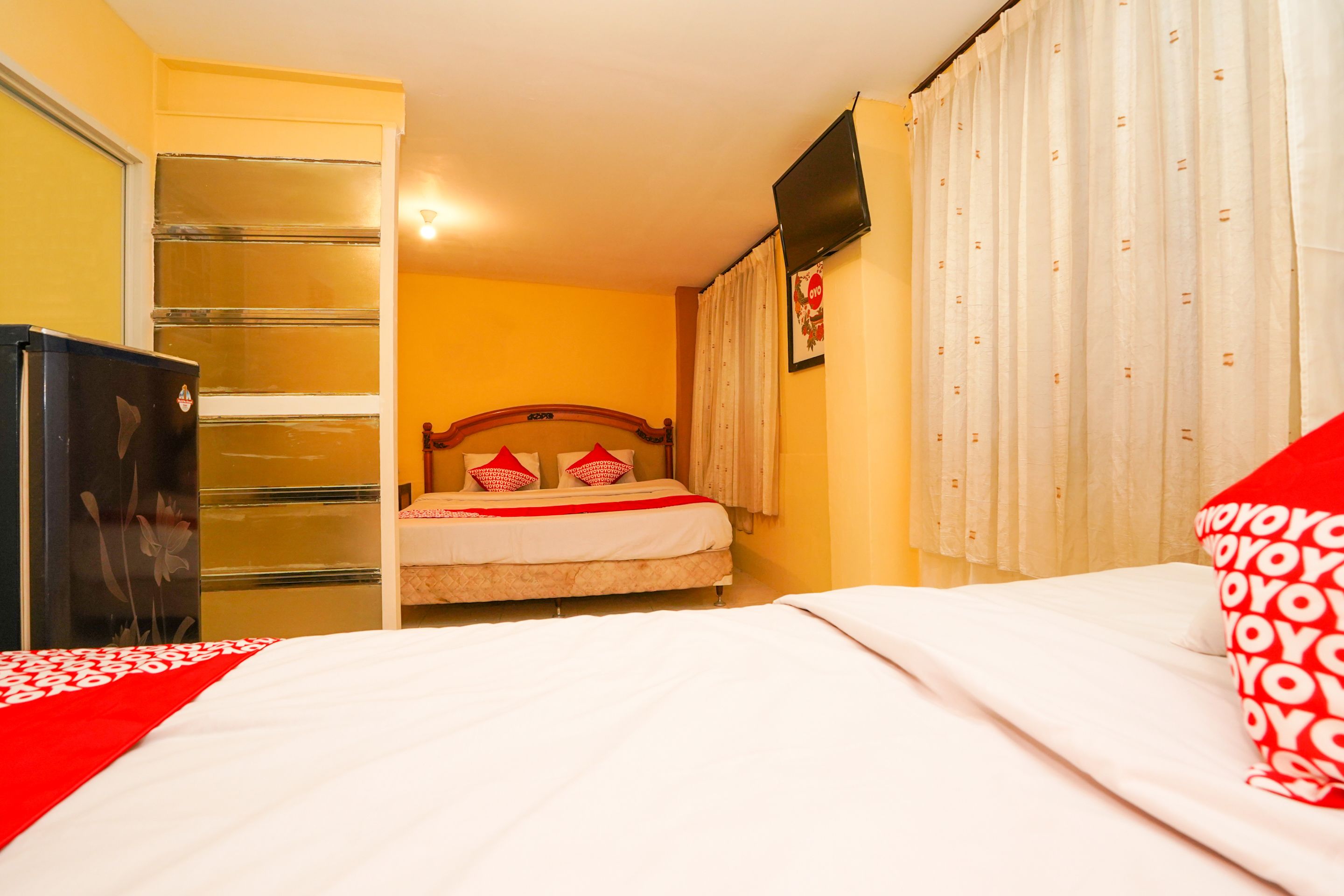 Een hotelkamer met een bed, een kledingkast, een televisie en een raam met gordijnen.