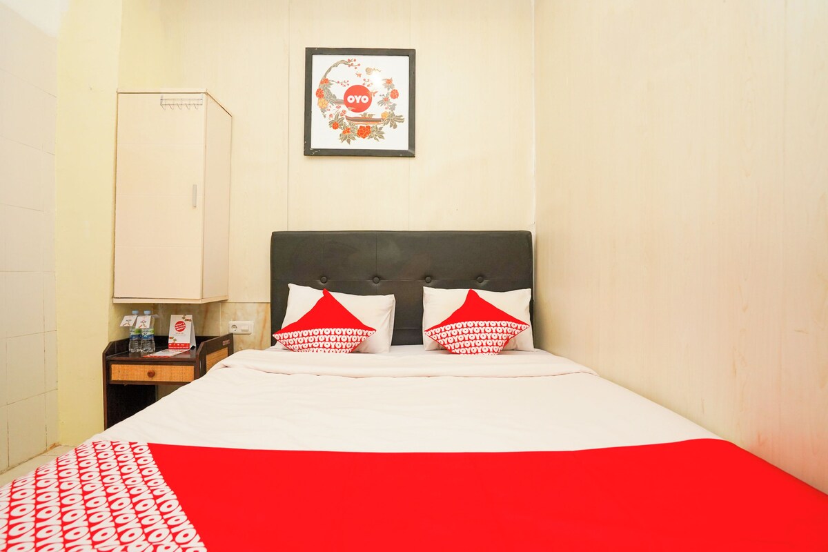 Une chambre d’hôtel avec un lit, une table de chevet sur laquelle se trouve une bouteille et un panneau, une armoire et un tableau encadré au mur.