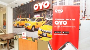 L’intérieur d’un hôtel, avec un comptoir d’accueil, une grande enseigne OYO Hotels et un présentoir promotionnel pour l’application OYO.