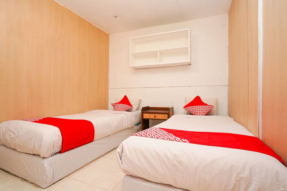 Habitación de hotel con dos camas individuales, cada una con colcha y almohadas rojas y blancas. Hay una mesita de noche de madera entre las camas con un cajón.