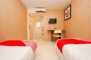 Ein Hotelzimmer mit zwei Betten, einem Schreibtisch, einem Sessel, einem Fernseher und einer Klimaanlage.