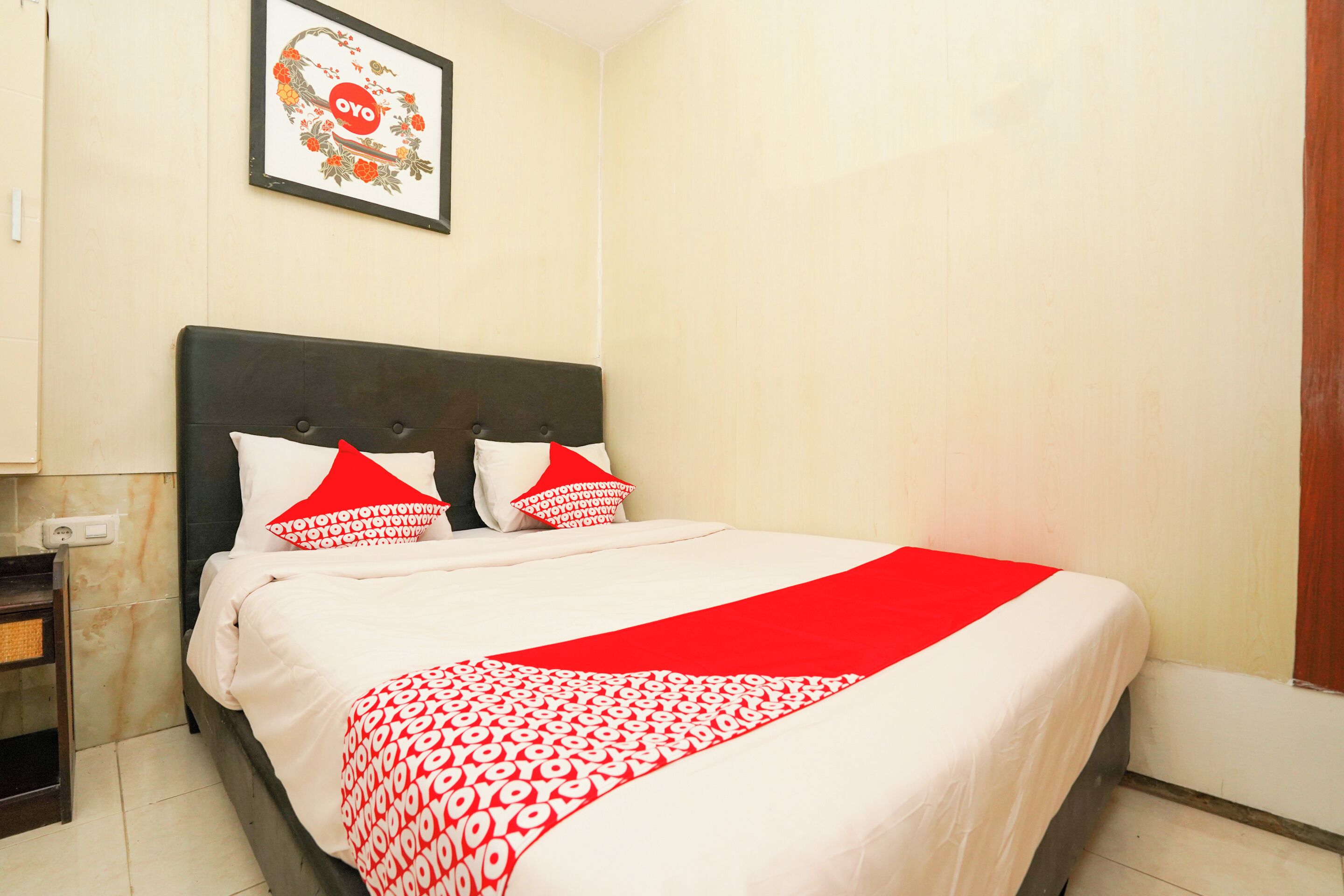 Un lit bien fait, recouvert d’une couvre-lit à motifs rouges et blancs, avec une tête de lit sombre et deux oreillers aux motifs rouges et blancs.