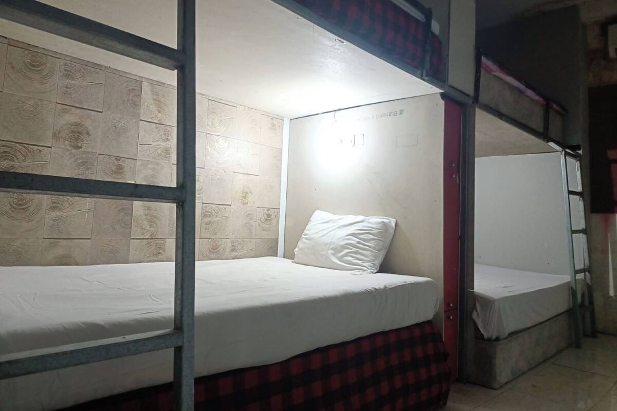 Un dormitorio con literas, una colcha roja y negra a cuadros y una almohada blanca.