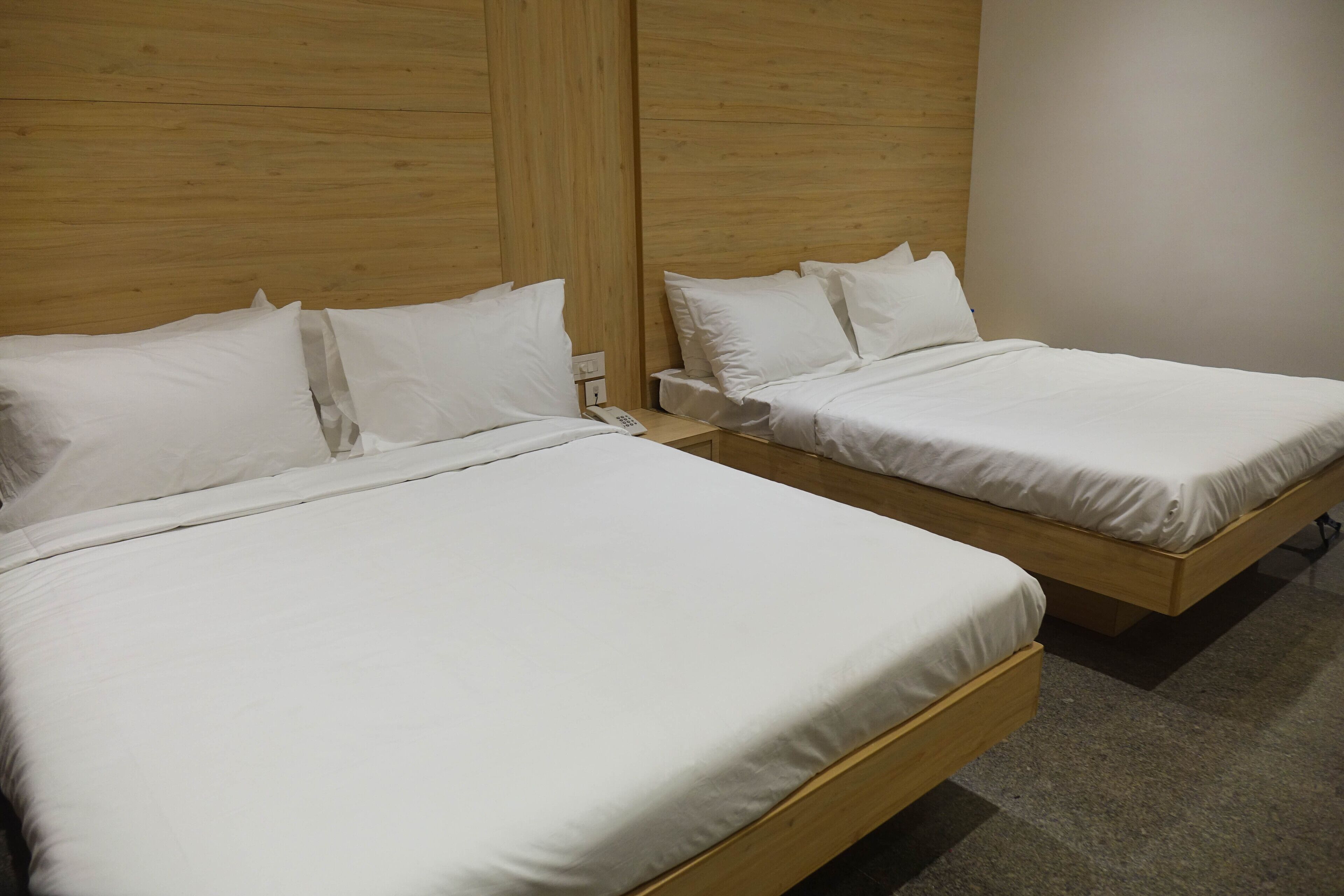 Two single beds with wooden headboards and white bedding in a room with a neutral color palette.