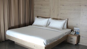 A neatly made bed with white linens, a wooden headboard, and a nightstand with a phone and water bottles. - Hotel Abis Grand (Coimbatore)