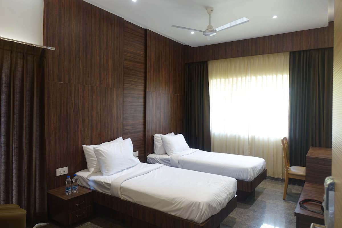 A hotel room with two single beds, a desk, a chair, a nightstand with a lamp, and a ceiling fan.