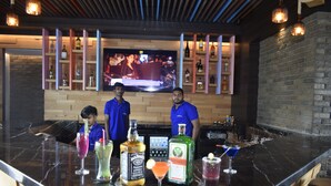 A bar area with a TV screen, shelves with bottles, and a counter with drinks. - Hotel Abis Grand (Coimbatore)