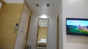 A hotel room with a wooden wardrobe, a bed, a mirror, and a TV on the wall. - Hotel Abis Grand (Coimbatore)