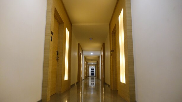 A long, narrow hallway with a polished floor and walls featuring a light wood finish. - Hotel Abis Grand (Coimbatore)