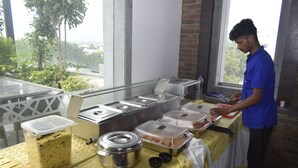 A buffet setup with various food containers and a person serving food. - Hotel Abis Grand (Coimbatore)