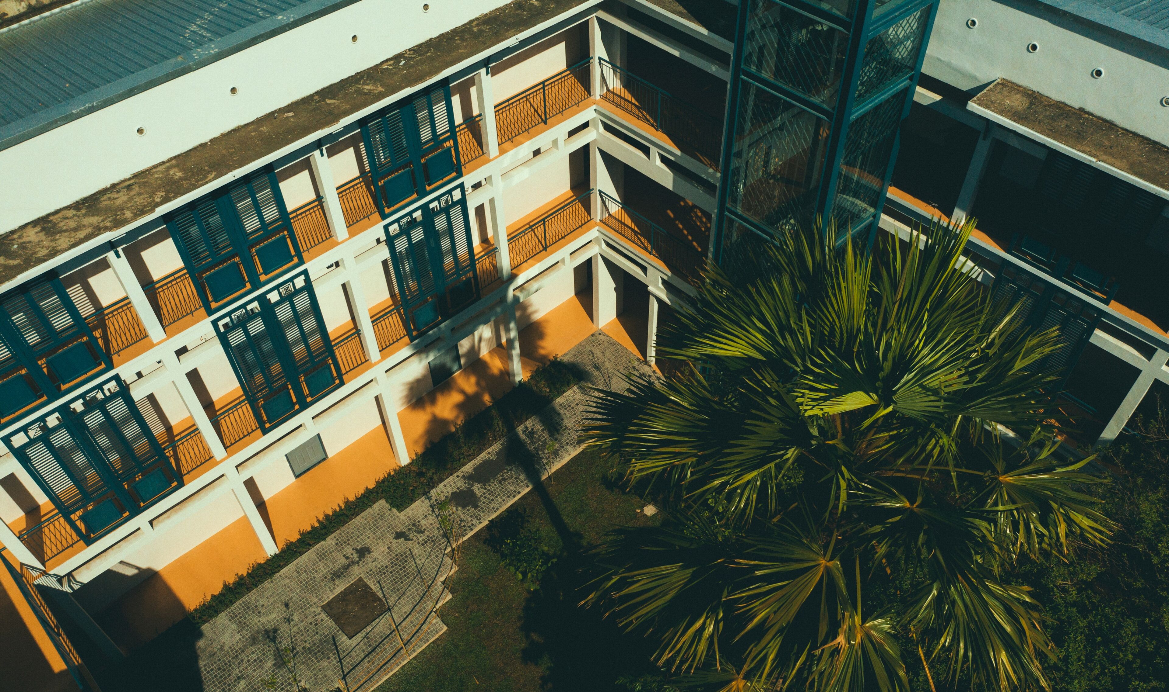 A multi-story building with balconies, a central courtyard, and a large palm tree.