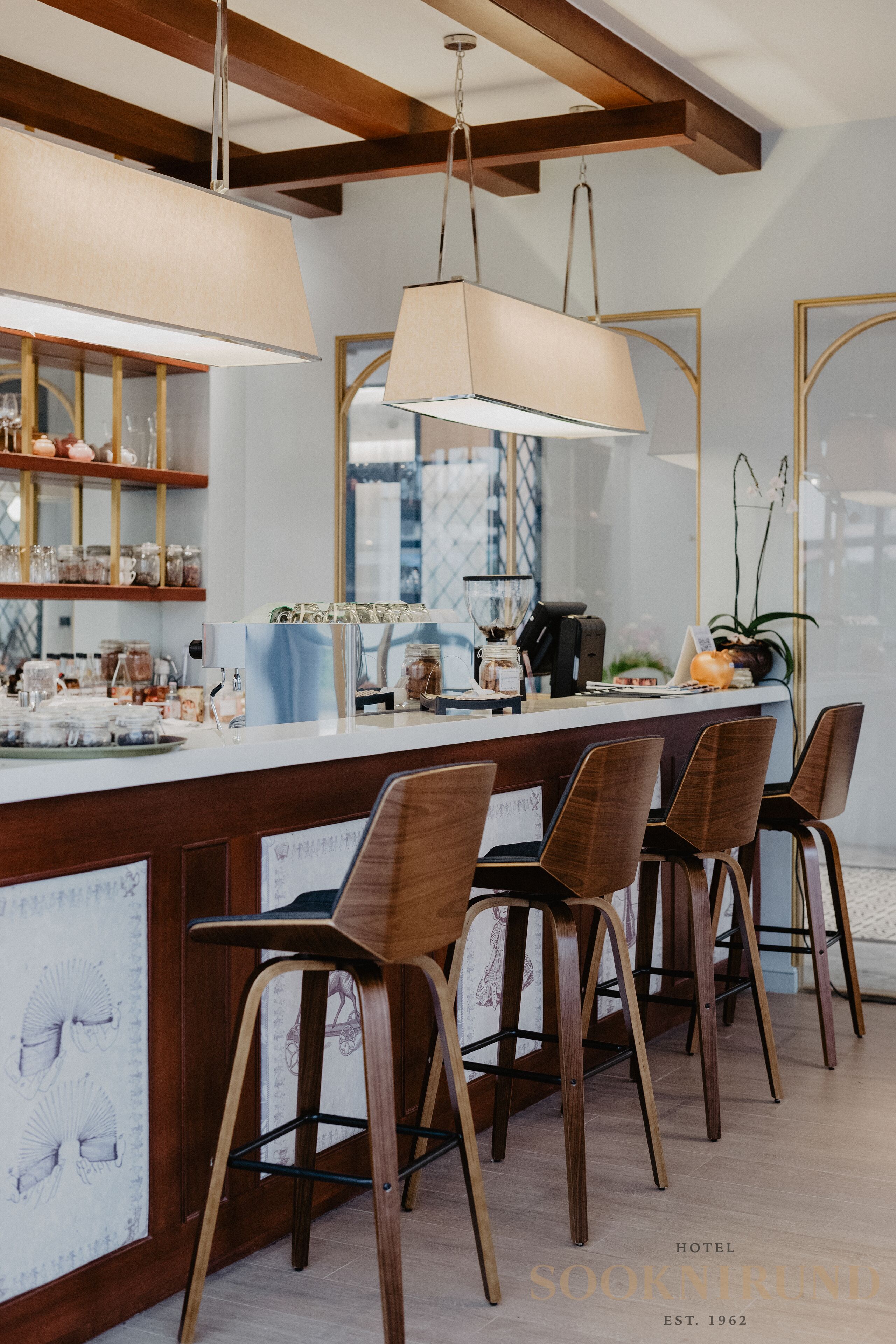 Uma área de bar com cadeiras de madeira, um balcão com diversos itens e luminárias pendentes.