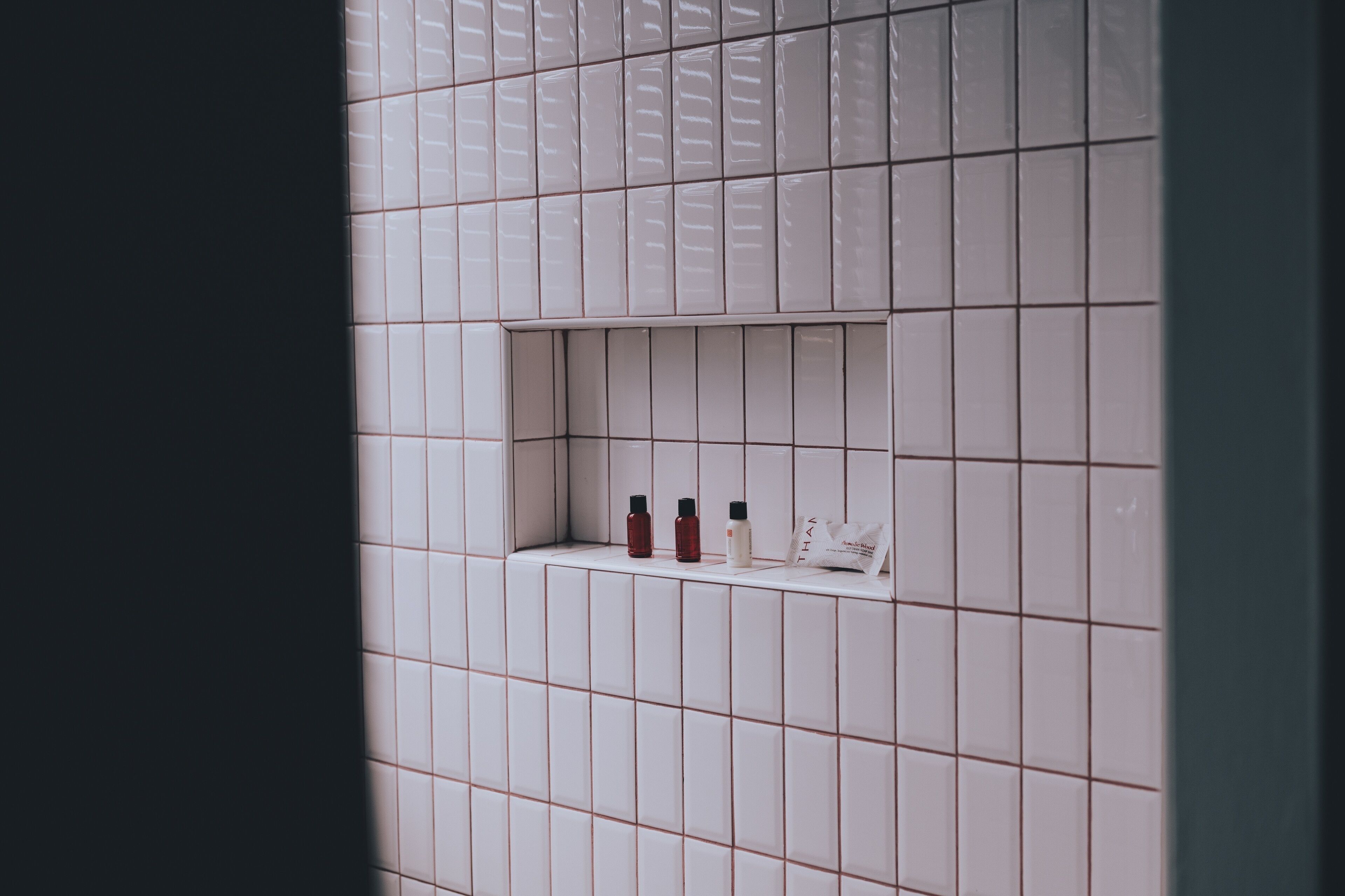 Un baño con paredes de azulejos blancos y una repisa con artículos de tocador.