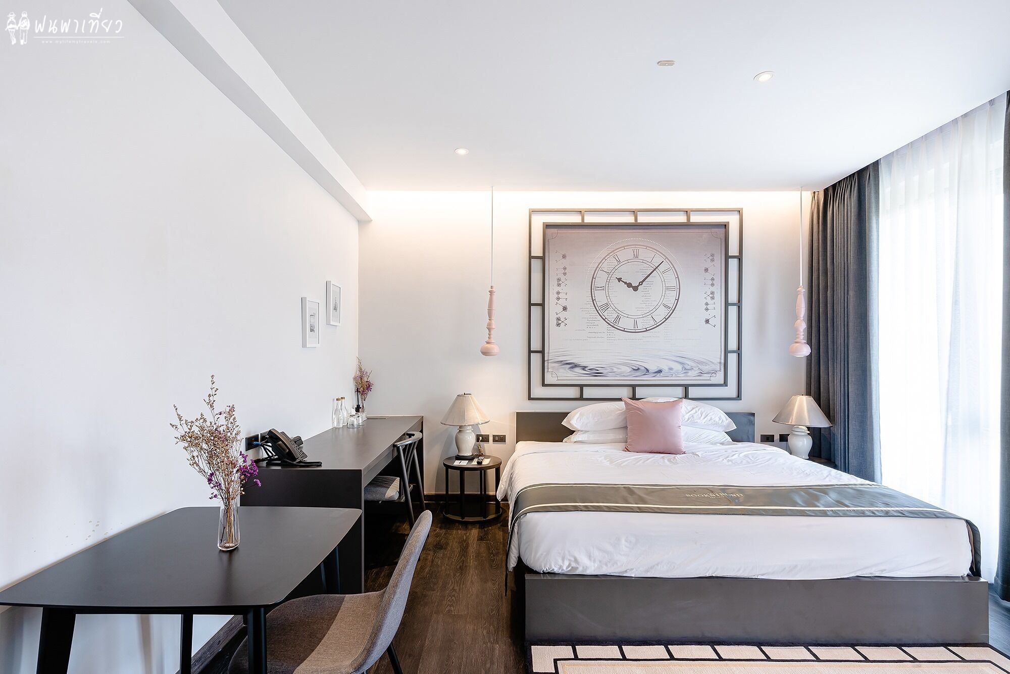 A modern hotel room with a large bed, bedside tables, a desk, and a wall-mounted clock.