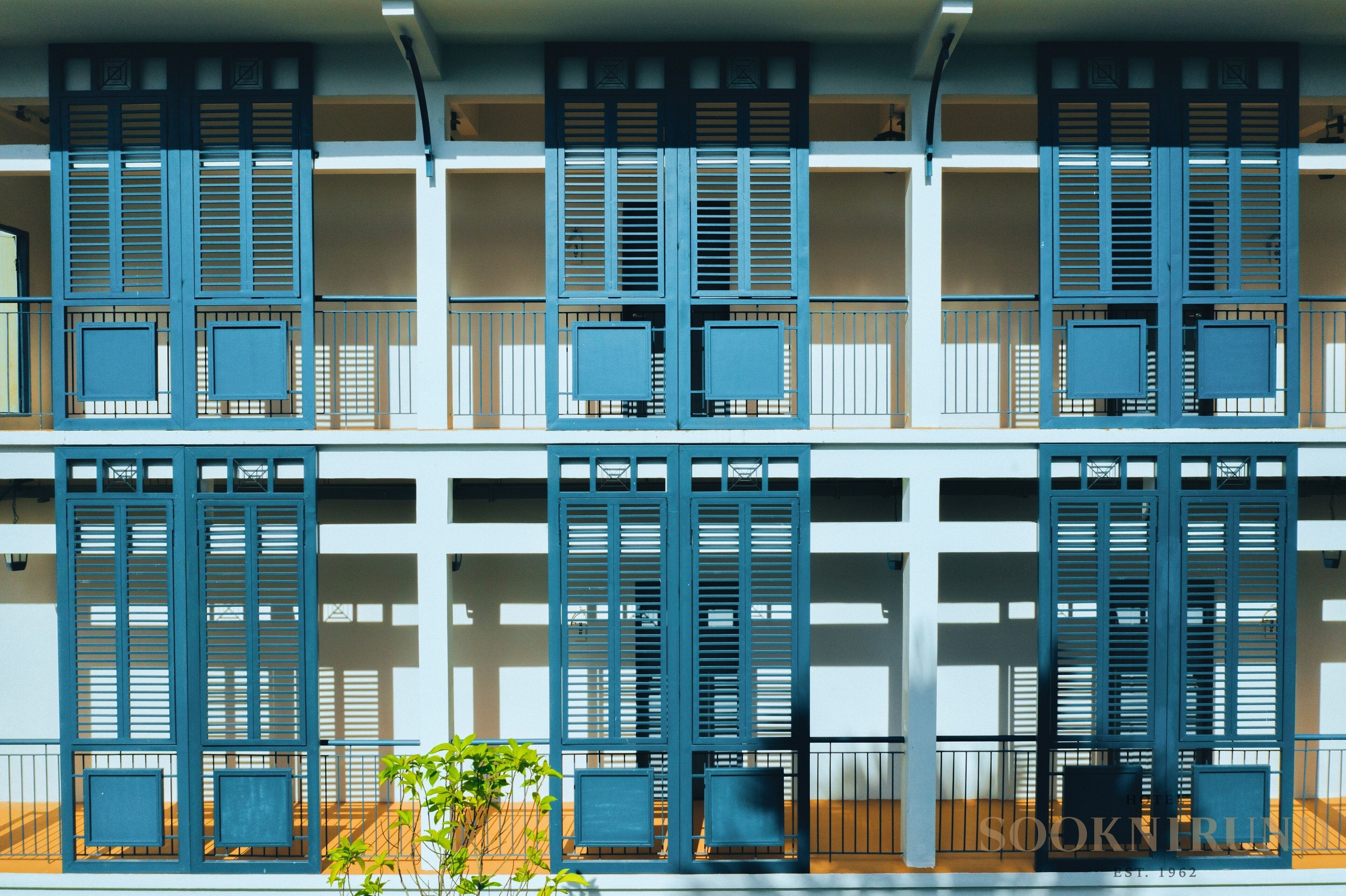A multi-story building with balconies, each featuring blue shutters and metal railings.