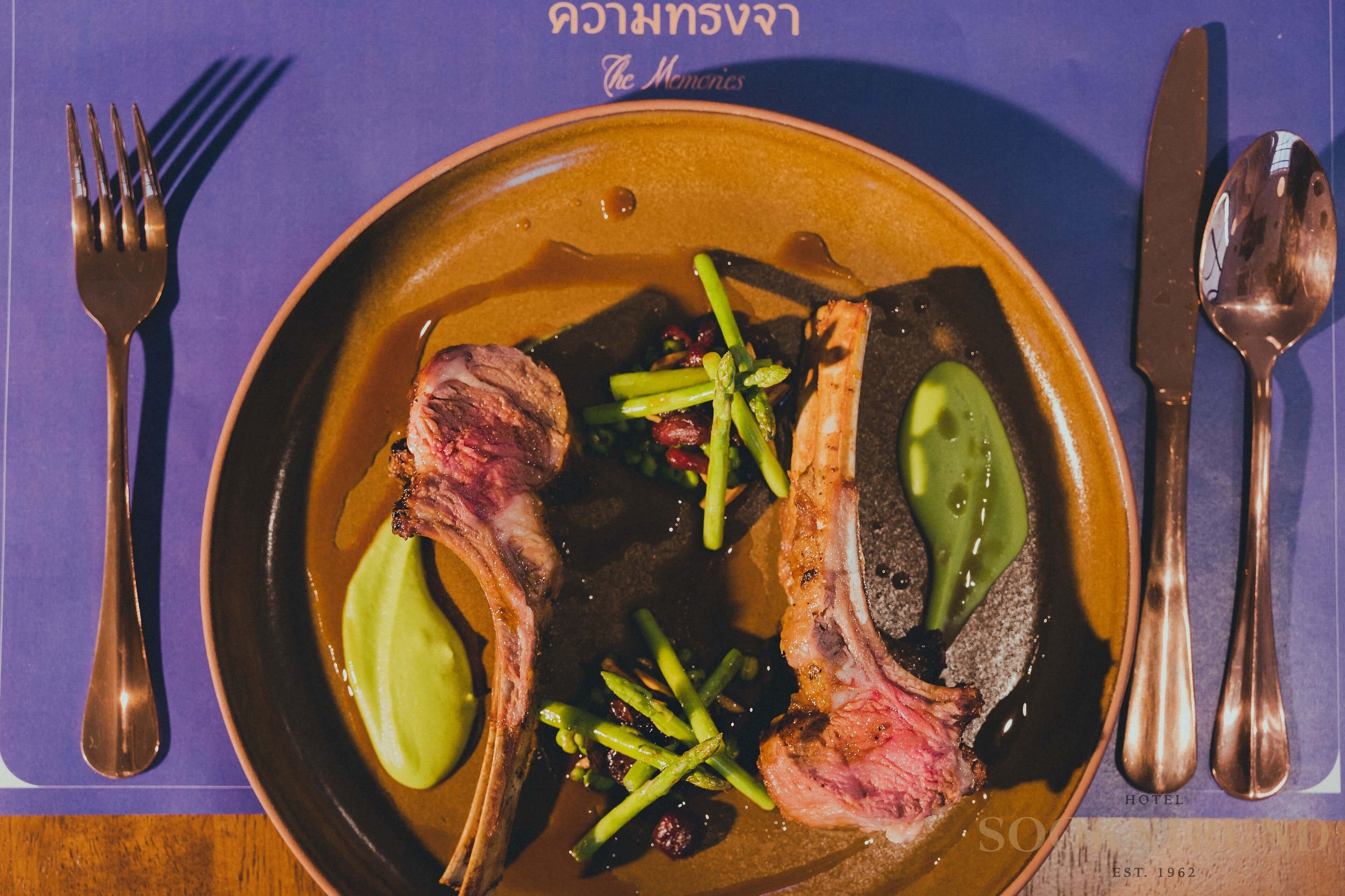 A plate with lamb chops, green beans, and a slice of green apple on a brown plate.