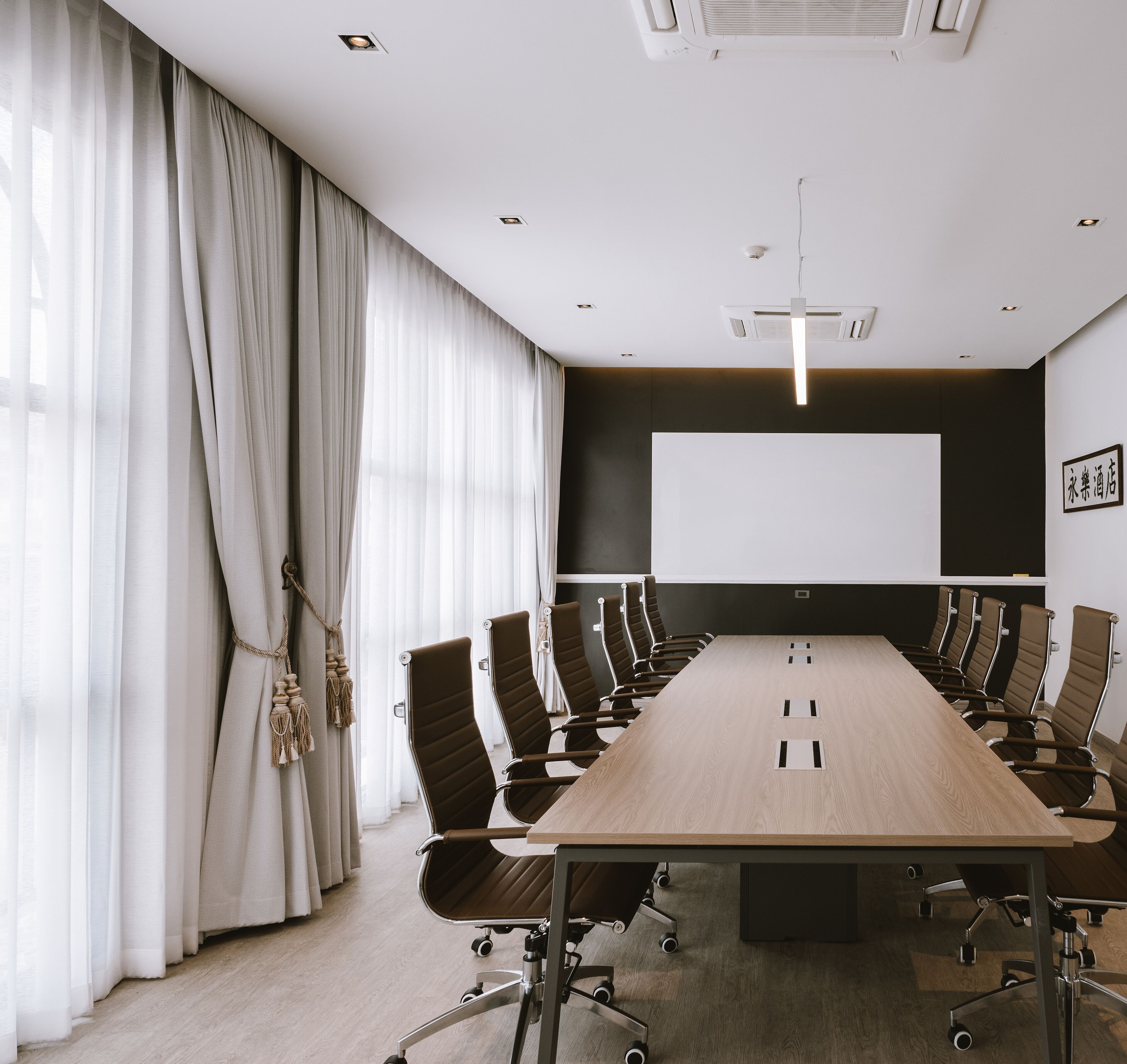 A conference room with a long table, brown chairs, a projector screen, and a whiteboard.