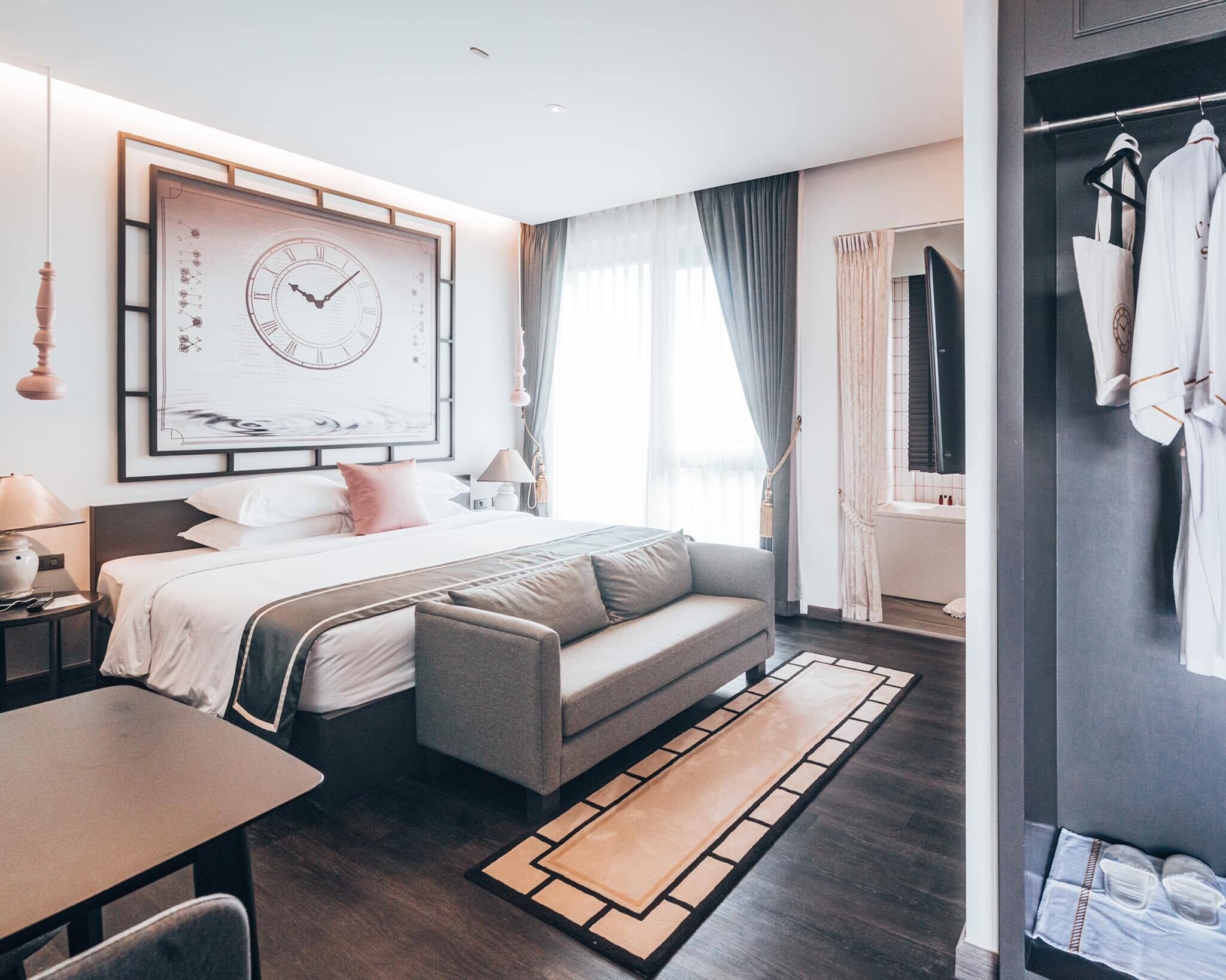 Une chambre d’hôtel moderne dotée d’un grand lit, d’un canapé, d’un bureau et d’une salle de bain visible à travers une porte en verre.