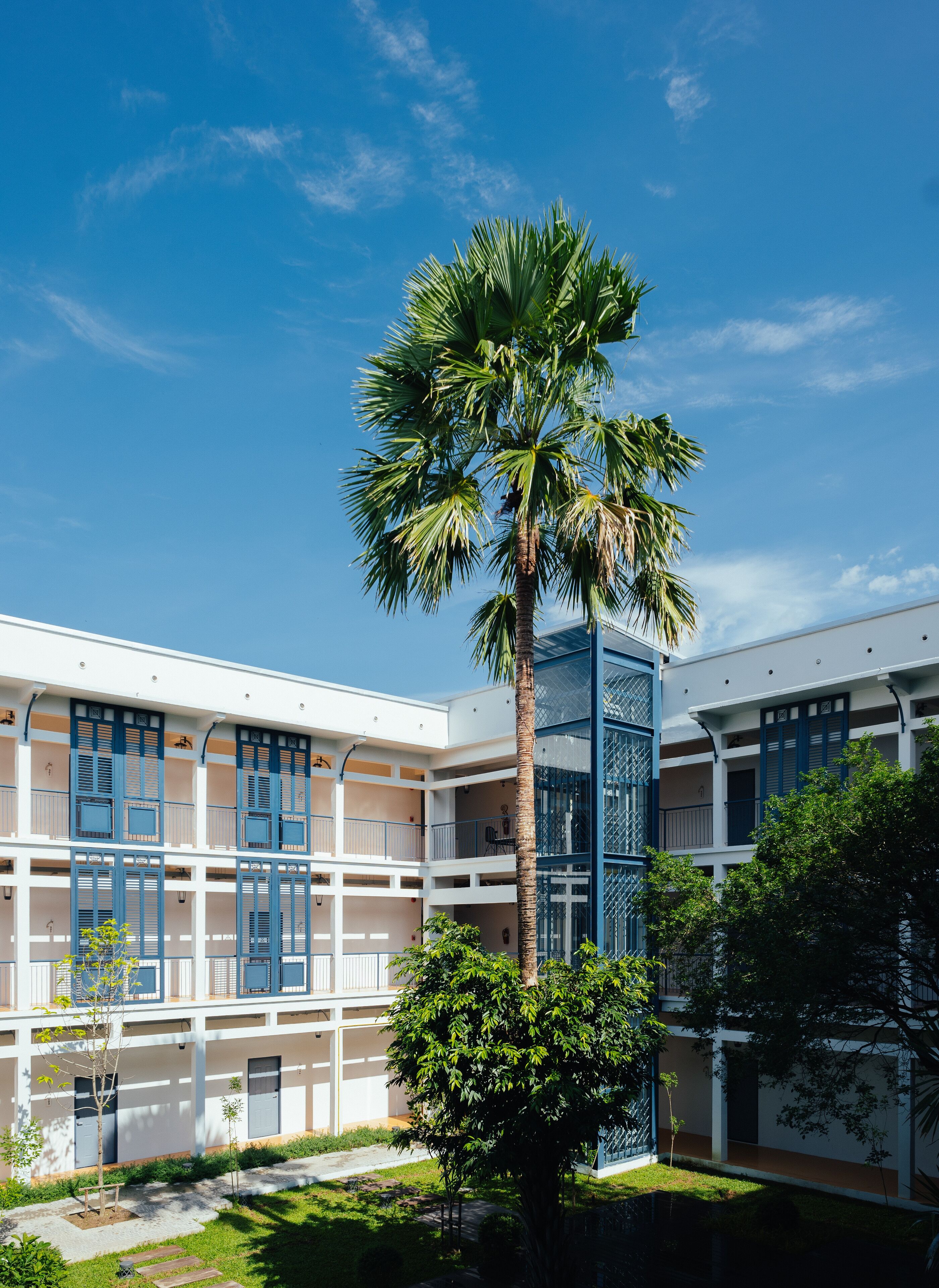 A multi-story building with a central courtyard featuring a palm tree and a smaller tree.