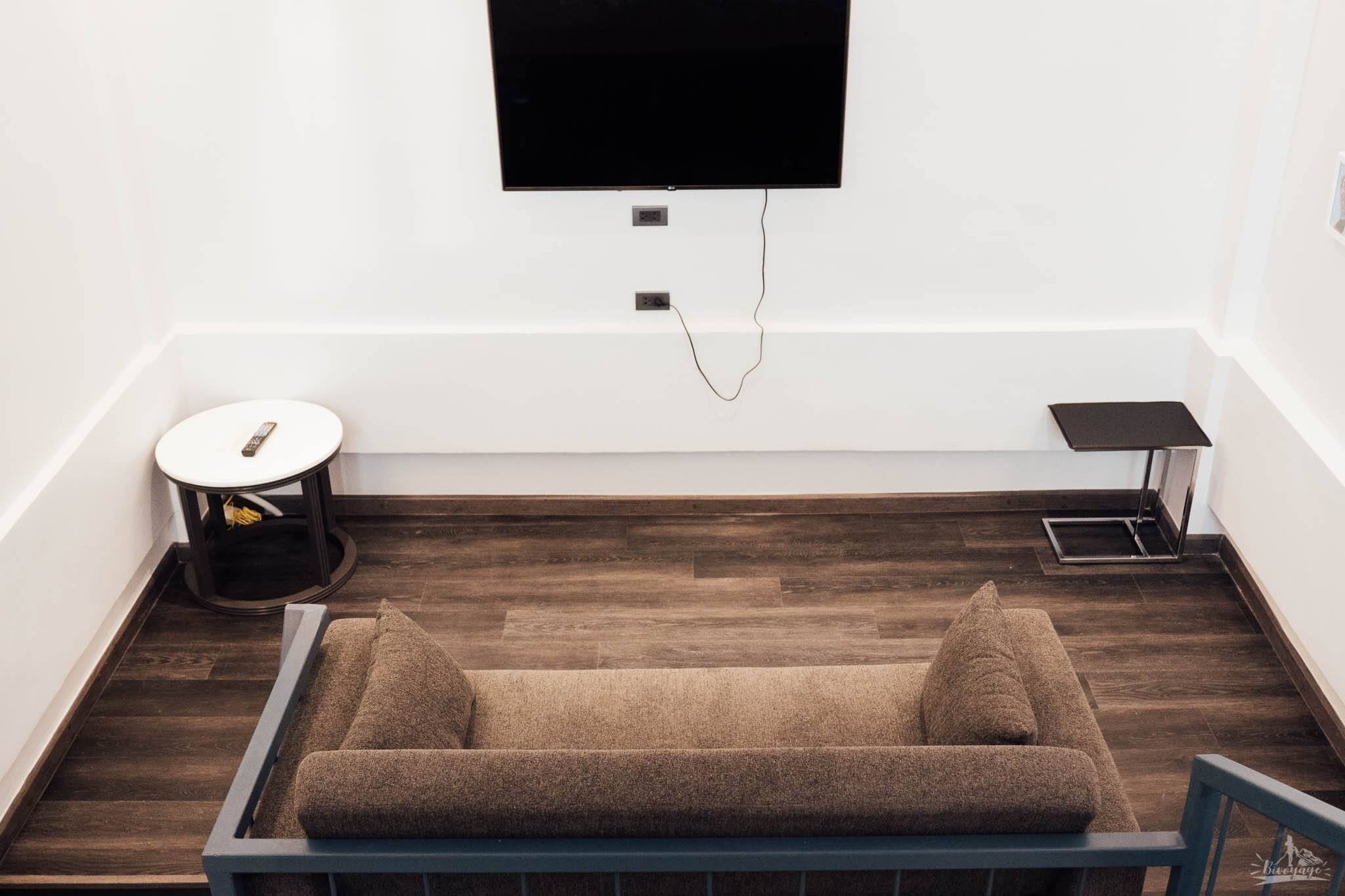A modern room with a wooden floor, a sofa, a small round table, and a flat-screen TV mounted on the wall.