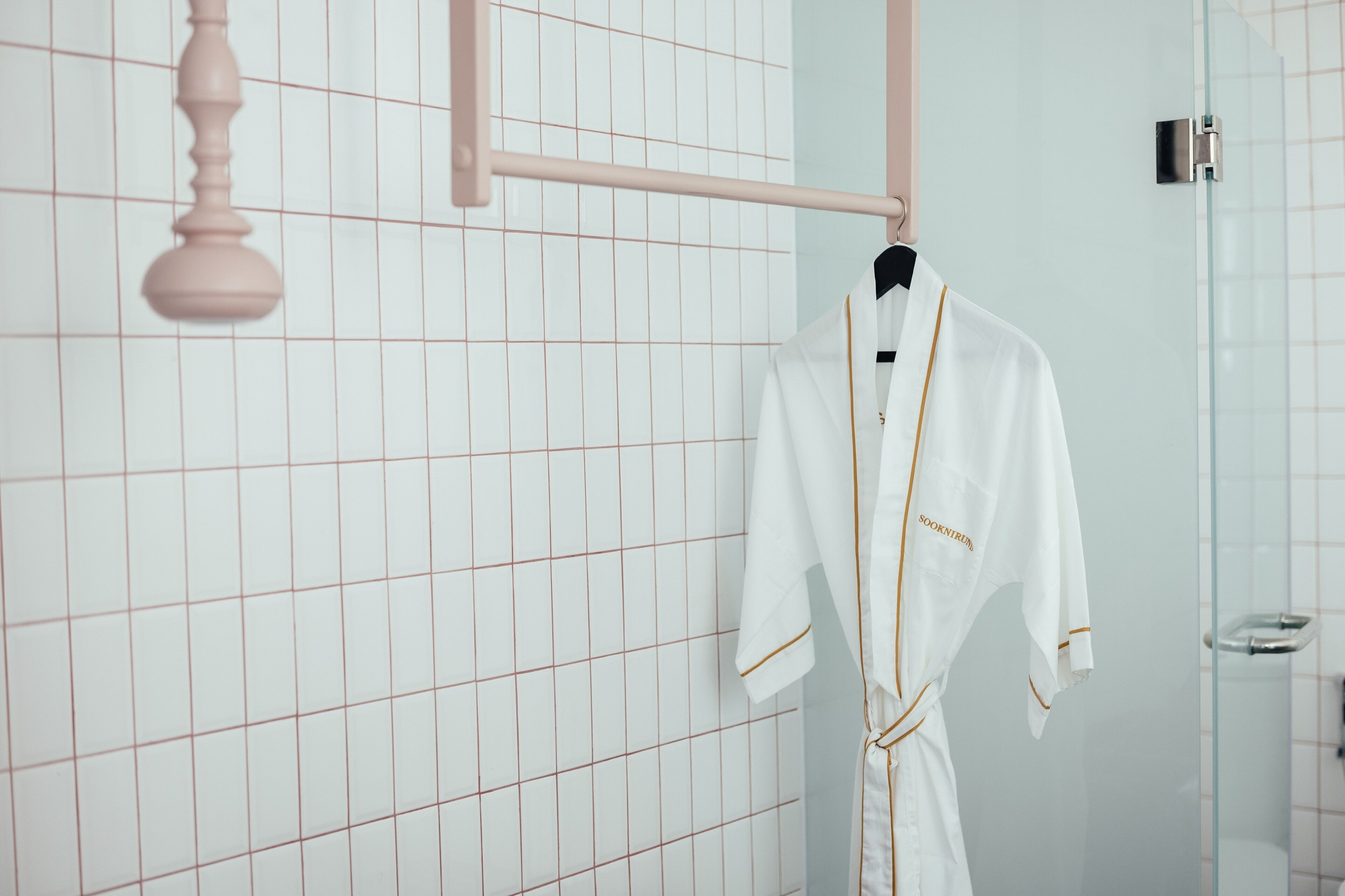 A white robe hanging on a rack in a bathroom with a grid-patterned wall and a glass shower enclosure.
