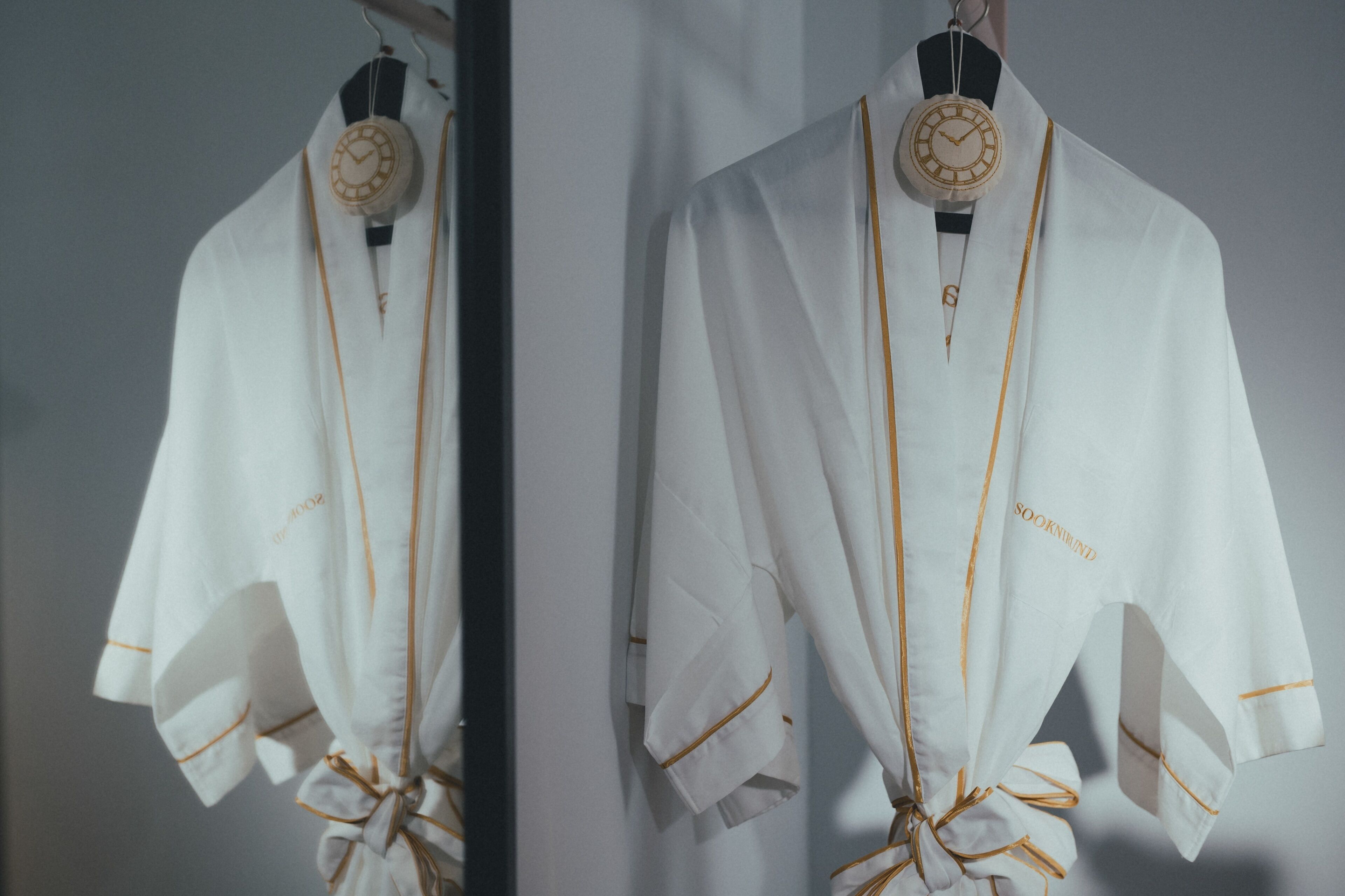 Two white robes with gold trim and a clock pendant, hanging on a rack.