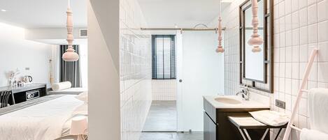 Una habitación de hotel moderna con cama, mesita de noche, lámpara y vista al pasillo que lleva al baño.