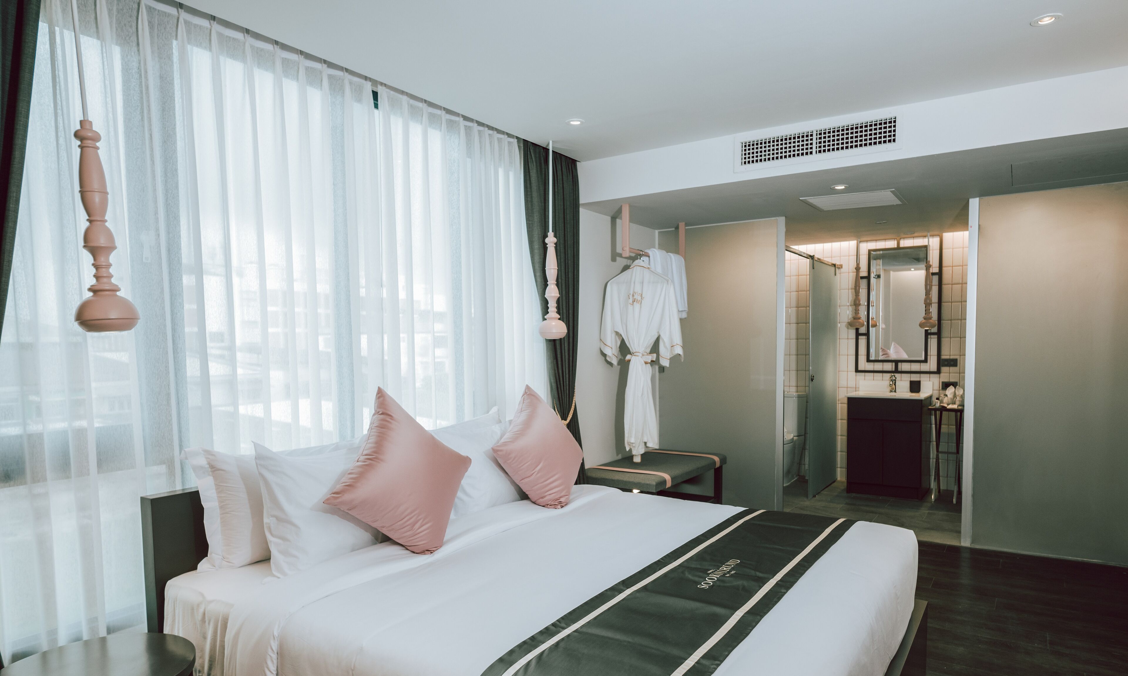 Ein Hotelzimmer mit einem großen Bett, einem Nachttisch, einem an der Wand hängenden Bademantel und einem durch eine offene Tür einsehbaren Badezimmer.