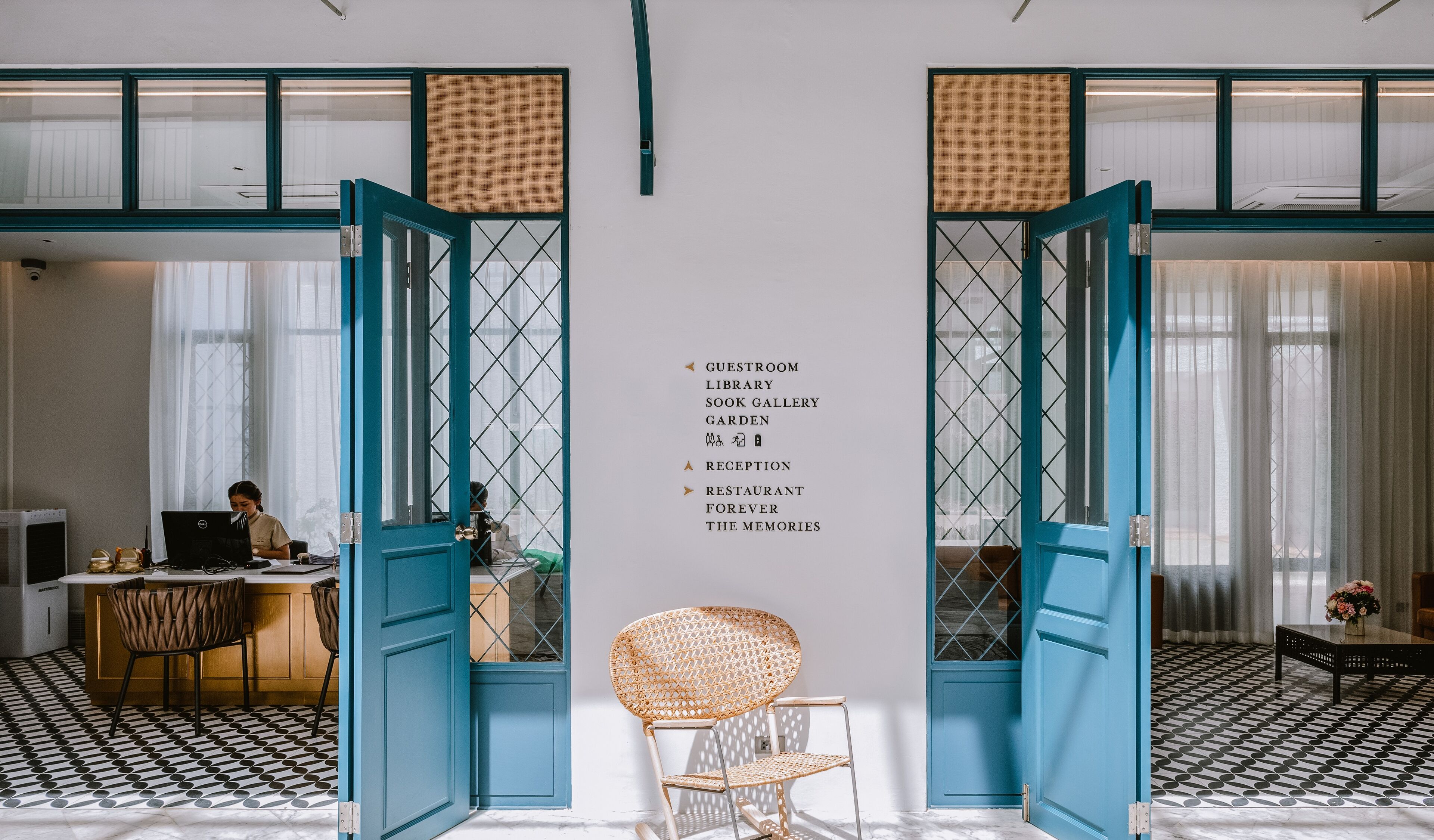 Un vestíbulo de hotel con puertas abiertas que dan acceso a diversas comodidades, como habitaciones de huéspedes, una biblioteca y un jardín.