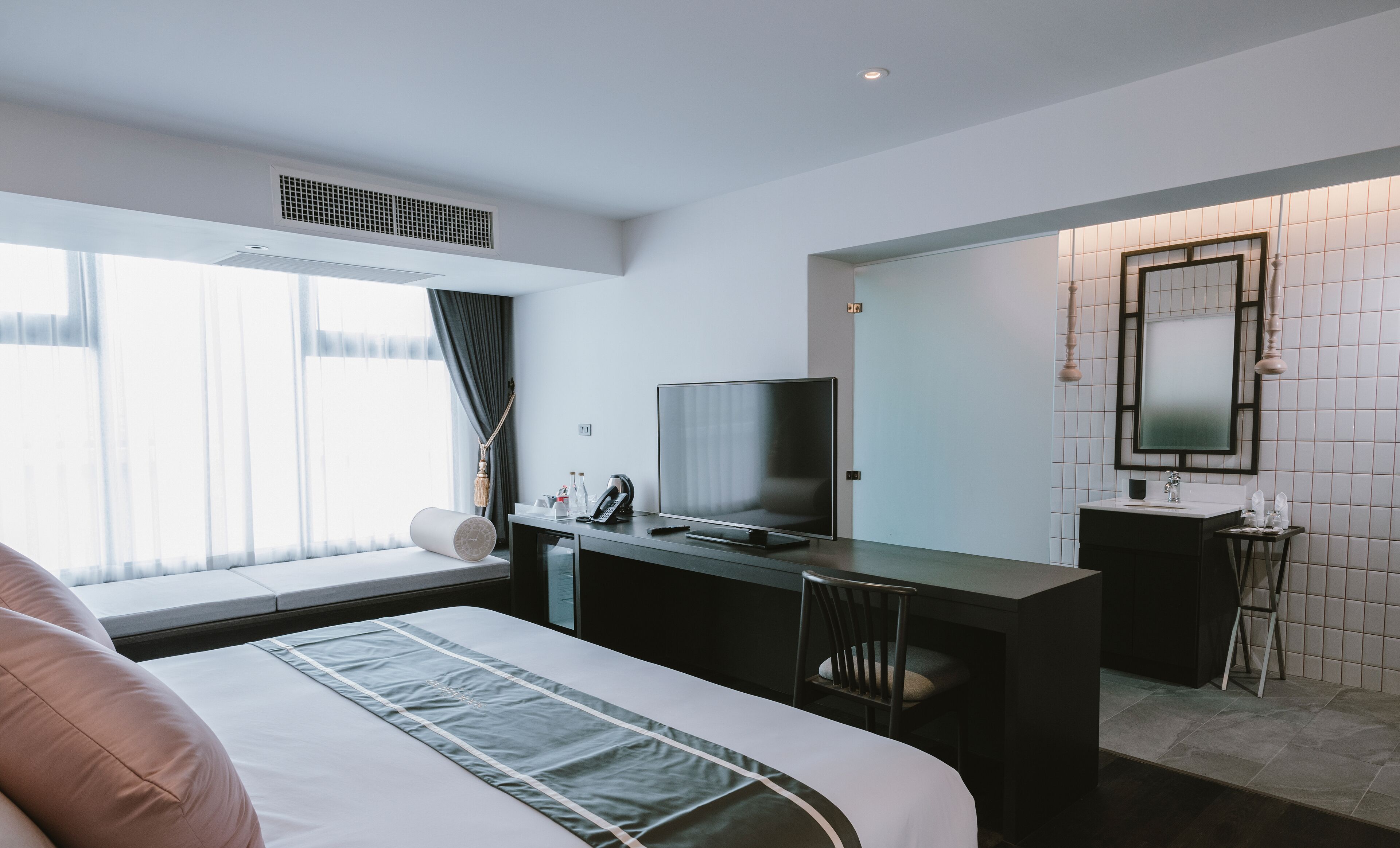 Hotelkamer met een bed, bureau met televisie, stoel, bureaulamp, telefoon en een badkamer met spiegel en wastafel.