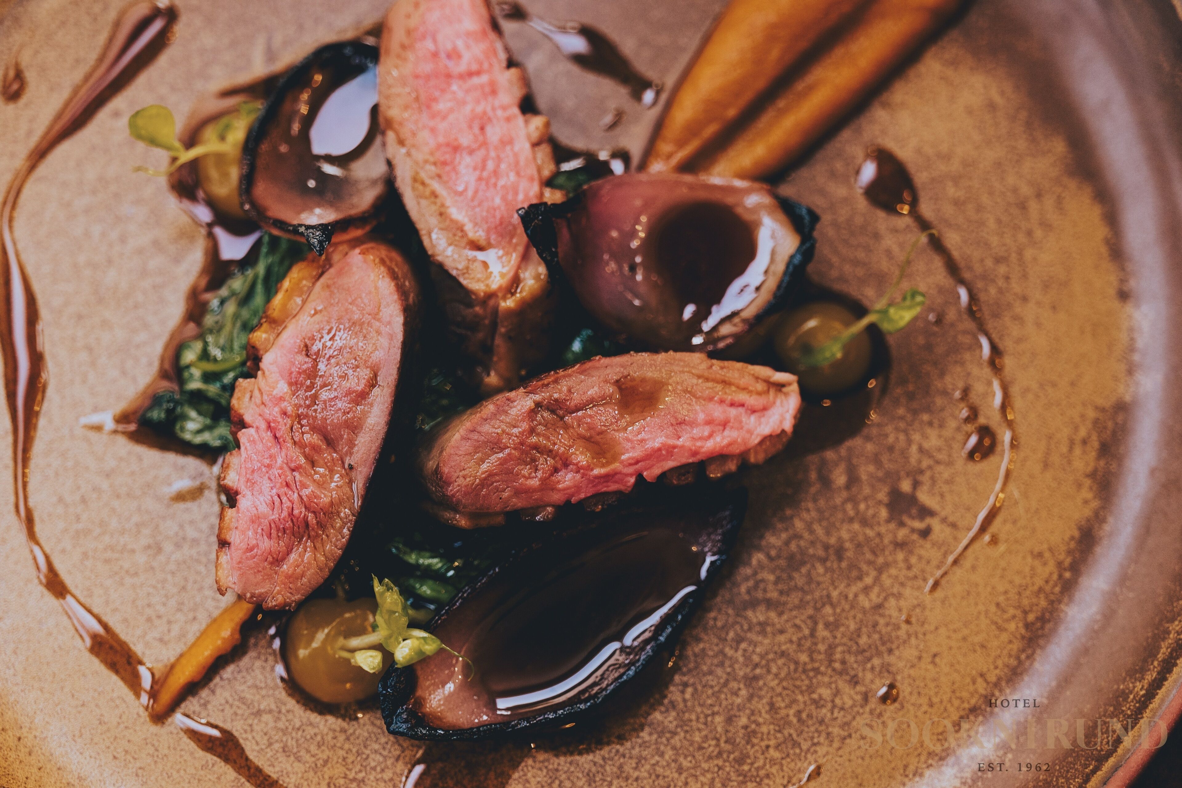 A close-up of a dish with mussels, meat, and greens, served on a plate with a textured surface.