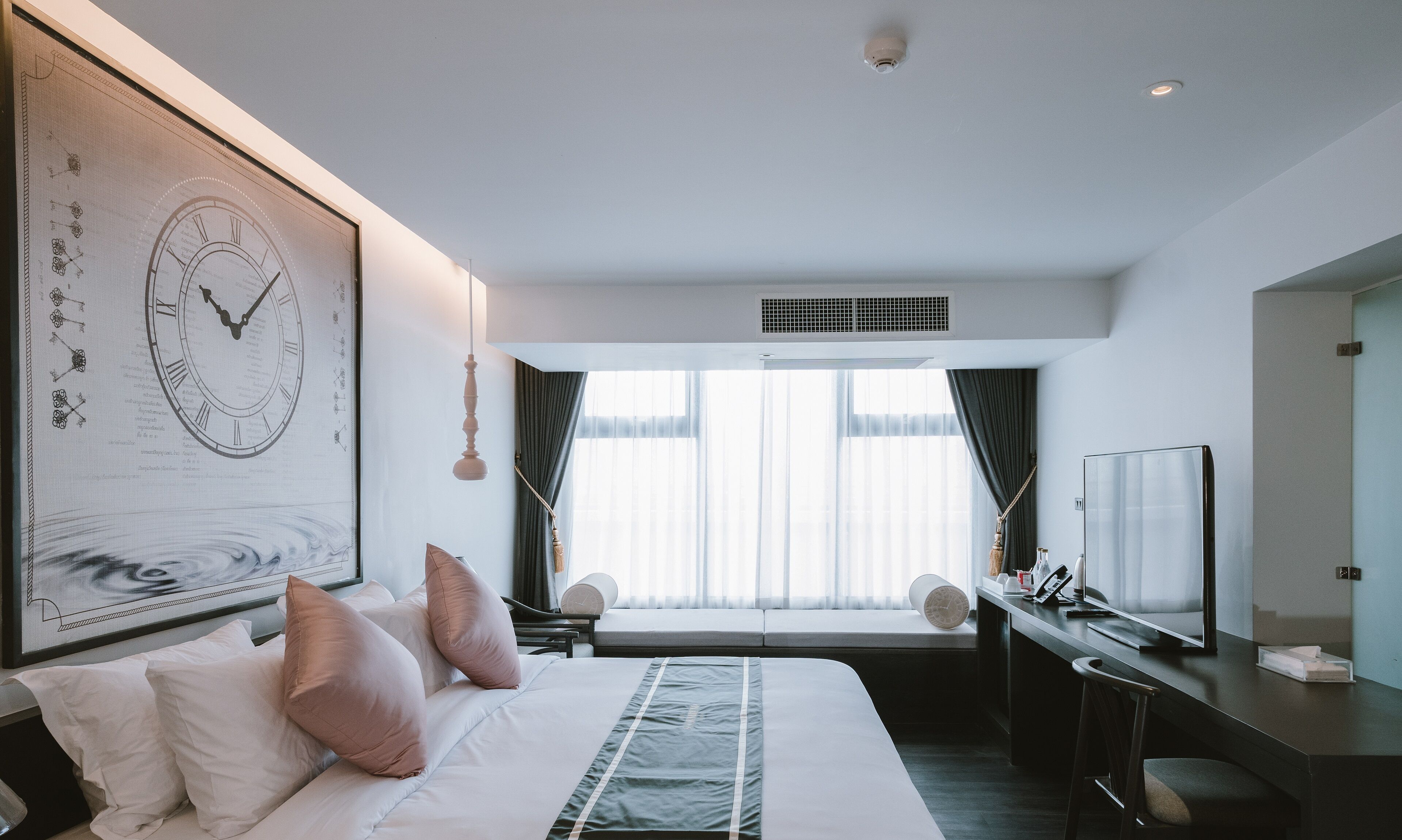 A modern hotel room with a large bed, a desk, a television, and a window with curtains.