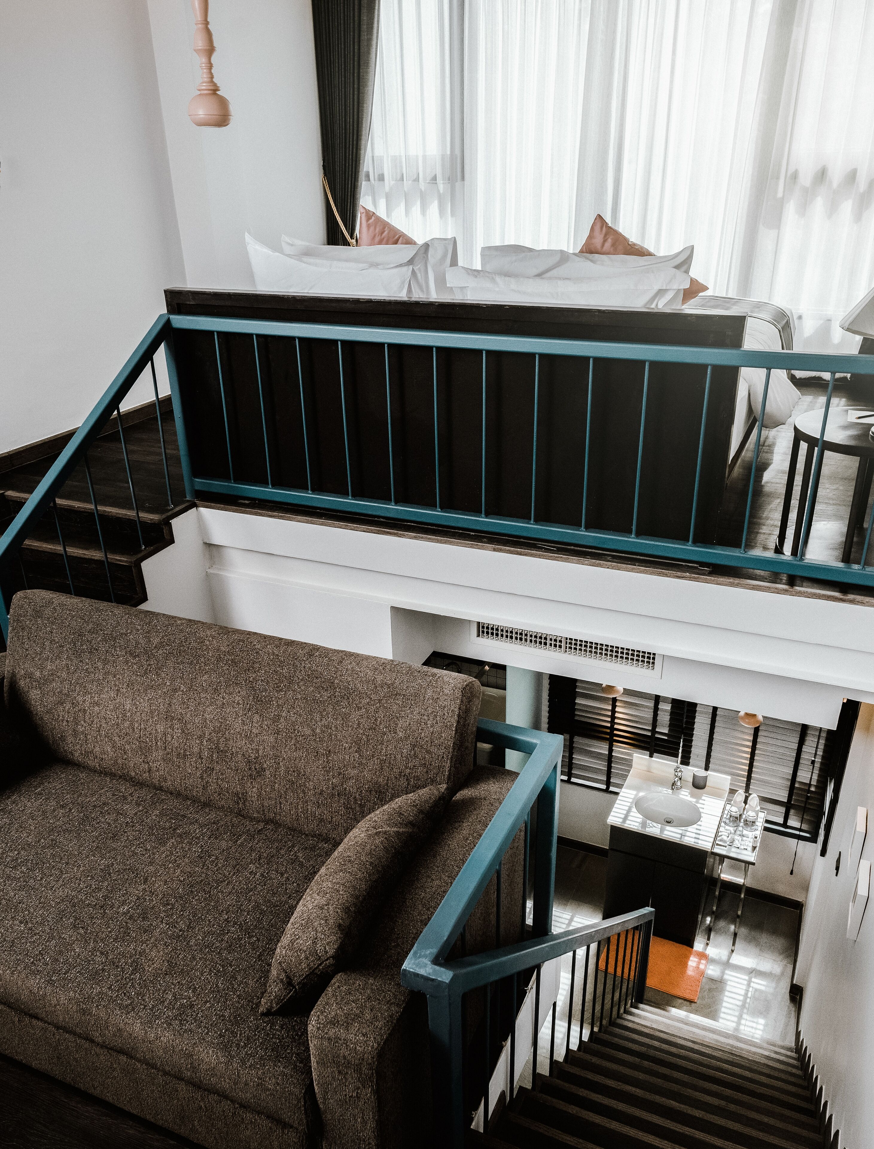 A modern interior with a staircase leading to a loft bedroom, a sofa, and a small table with a sink.